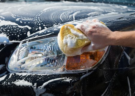 Man washing a soapy car with a yellow sponge.