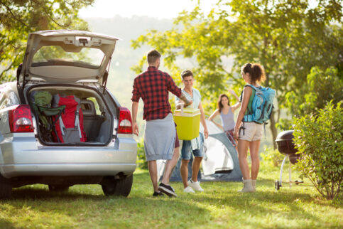 friends unpacking car for camping trip in countryside